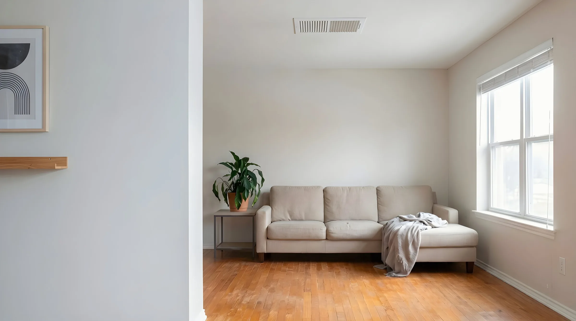 The same living room, now cool and evenly lit, blinds open, the fan gone.